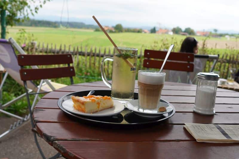 Ein gedeckter Tisch - mit einem Stück Kuchen, einem Milchkaffee, einem Zitronengetränk, einem Zuckerglas und einer Speisekarte
